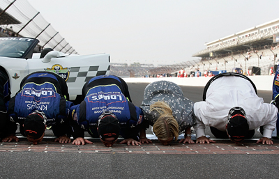 (L-R): Crew chief Chad Knaus, Jimmie Johnson, Chandra Johnson and owner Rick Hendrick kiss the yard of bricks after winning the Allstate 400 at the Brickyard. (Photo Credit: Jason Smith/Getty Images for NASCAR)