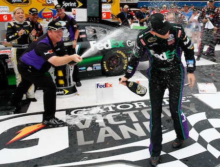 (Left to right) Crew chief Mike Ford sprays his driver Denny Hamlin in Michigan International Speedway's Victory Lane after winning the Heluva Good! Sour Cream Dips 400 Sunday in Brooklyn, Mich. (Credit: Geoff Burke/Getty Images for NASCAR)