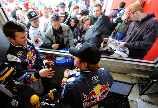 (Left to right) NASCAR Sprint Cup Series Red Bull Racing teammates Kasey Kahne and Brian Vickers talk as they sign autographs for fans in the garage area during Preseason Thunder testing on Friday at Daytona International Speedway in Daytona Beach, Fla. (Credit: Jared C. Tilton/Getty Images for NASCAR)