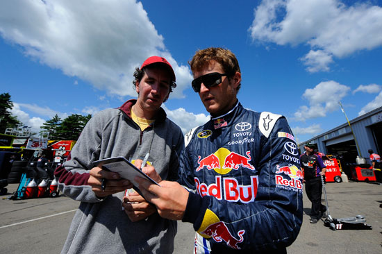 Kasey Kahne (right), driver of the No. 4 Red Bull Toyota, signs his autograph for a fan in the garage area during practice for the NASCAR Sprint Cup Series Heluva Good! Sour Cream Dips at the Glen at Watkins Glen International on Aug. 12 in Watkins Glen, N.Y. (Credit: Jason Smith/Getty Images for NASCAR)
