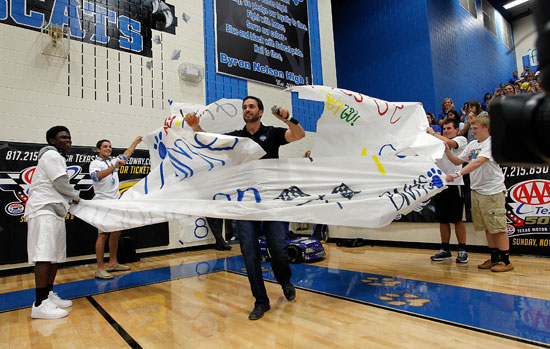 Five-time NASCAR Sprint Cup Series champion Jimmie Johnson breaks through a spirit banner during a Texas football-style pep rally at Byron Nelson High School on Wednesday in Trophy Club, Texas. (Credit: Tom Pennington/Getty Images for Texas Motor Speedway)